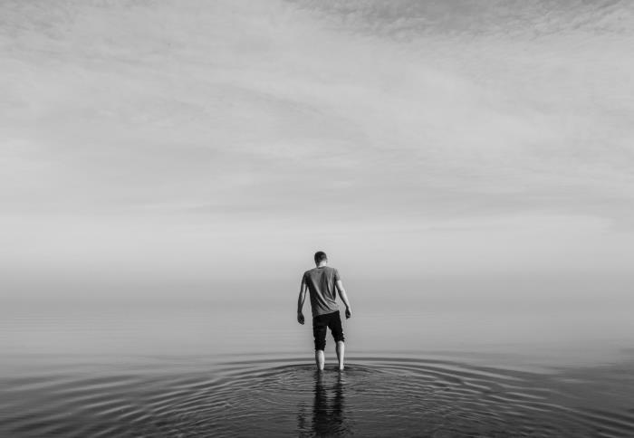 svartvitt porträtt av en ung man barfota i det lugna vattnet i havet, i bakgrunden horisonten gömd i dimman