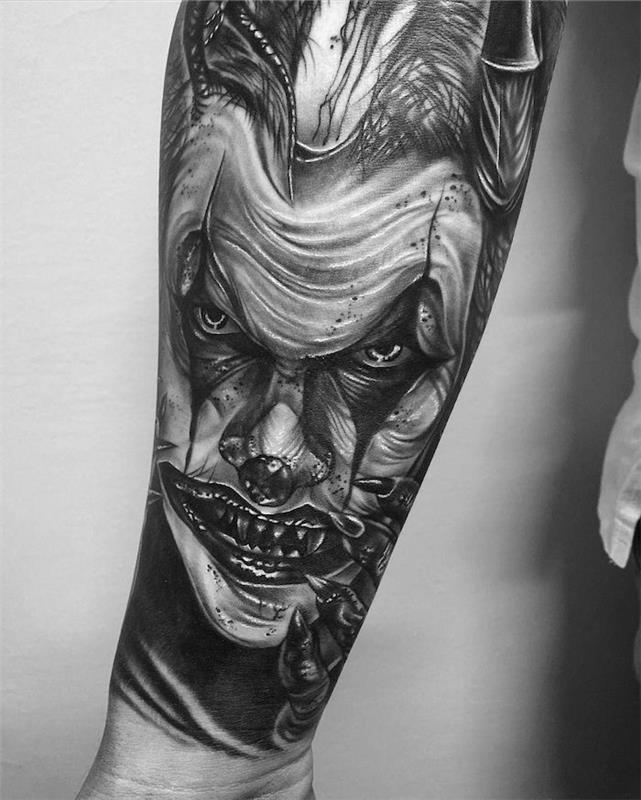 Tatuaggio braccio uomo con il disegno del viso di joker con la bocca aperta