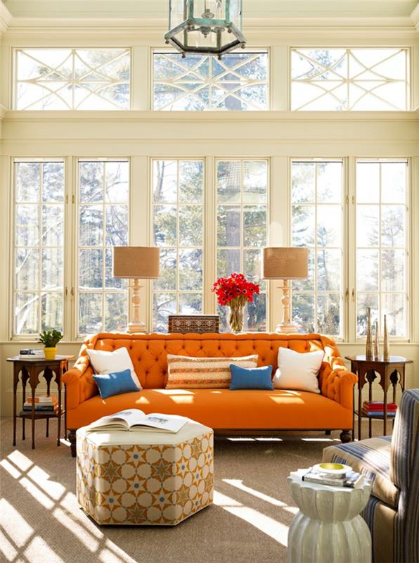 oranžová čalúnená pohovka, béžový puf, béžové stolné žiarovky, veľké okno, lampové stropné svetlo