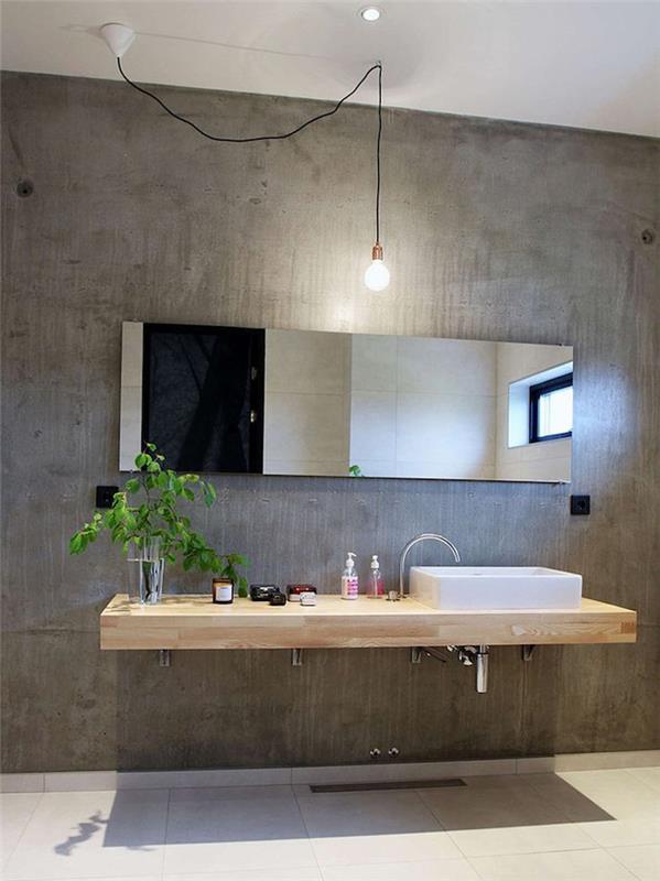 hrubá stena z voskovaného betónu pre dekor v priemyselnom štýle so závesnou drevenou umývadlovou skrinkou a dlažbou