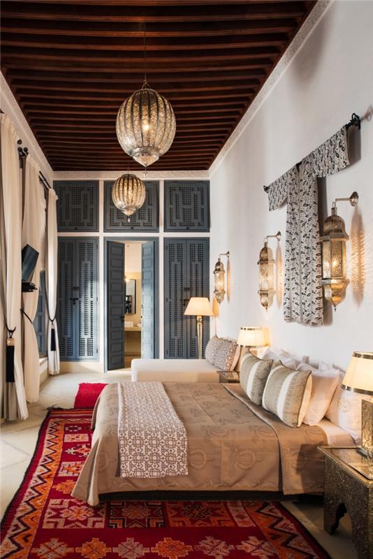 dekorácia malej spálne s vysokým stropom z tmavého dreva zariadená v marockom štýle, nápad na čelo postele s lampou a tradičným oblečením