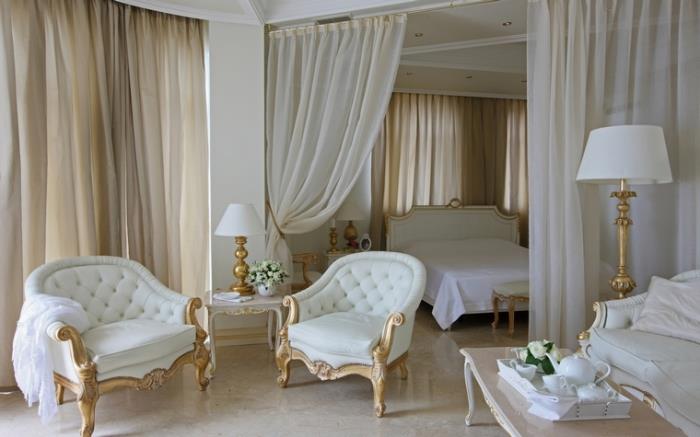 långa ecru gardiner i sovrum inredda i retro barockstil med vita och guldmöbler