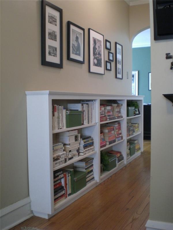 خزانة كبيرة بيضاء ، مع أرفف تحتوي على كتب وصناديق ، وعدة صور بأحجام مختلفة وأطر ملونة معلقة فوقها ، وأفكار لتزيين المدخل ، وأرضية خشبية.