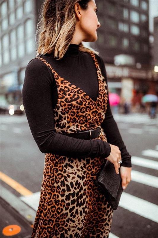 امرأة تقف في منتصف الشارع ، اتجاهات الموضة الخريفية ، ترتدي بلوزة بولو سوداء ، فستان بطبعة جلد الفهد في الأعلى