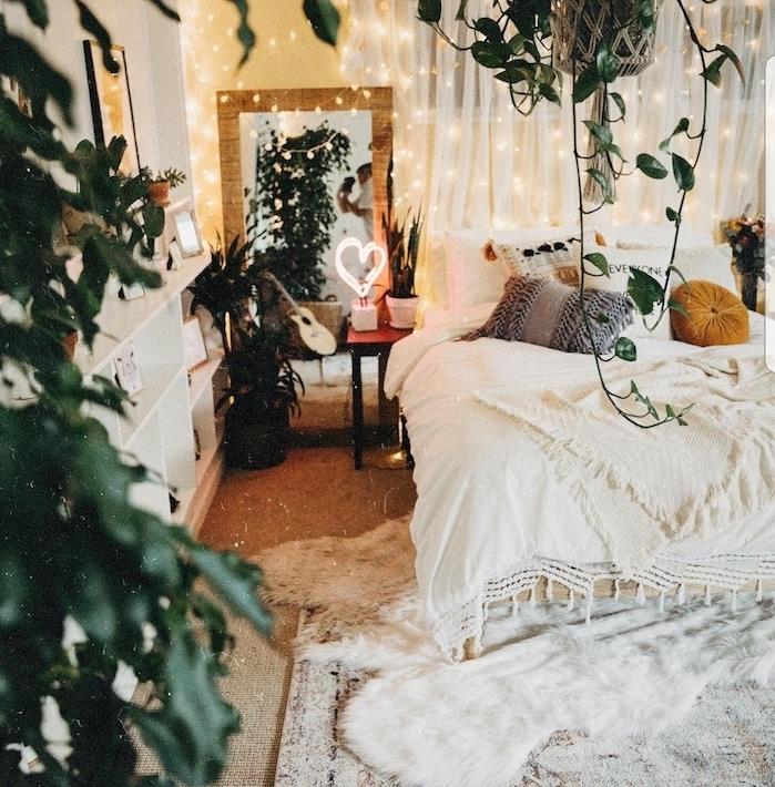 model bohémskej spálne s duchom džungle so závesnými rastlinami a črepníkovými rastlinami, posteľnou bielizňou a bielym kobercom, svetlými girlandami pre romantickú atmosféru