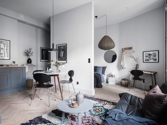 idé hur man ordnar en rymlig studio med ett sovrum åtskilt av en vägg, vardagsrum med svart skinnsoffa, runt soffbord, originalmatta, bord omgiven av skandinaviska stolar