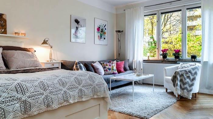 grå soffa och litet vitt designer soffbord på grå matta, grå fåtölj, säng i traditionell stil, ljusbeige väggar, dekorativa ramar