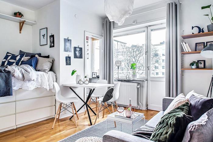 säng hatar överbelastning av dekorativa sängkläder och kuddar, skandinaviskt matbord och stolar, grå matta, grå soffa dekorerad med dekorativa kuddar, grå gardiner
