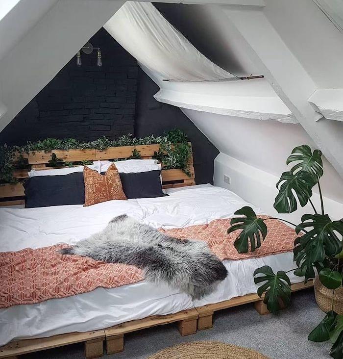 vnútorný brečtan a monstera deliciosa, bohémska šikmá výzdoba spálne s paletovou posteľou a paletovým čelom, biela posteľná bielizeň, červeno -biely pléd, koža zvierat, stena na čiernom pozadí