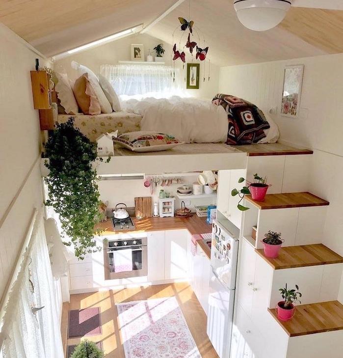 säng på andra våningen till vilken en trappa leder till en bous, sovplats under sluttningen, kompakt kök i trä och vitt