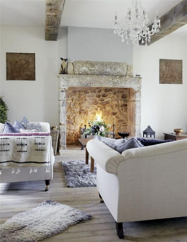 elegantný luster s javorovými bielymi pohovkami zdobený kokonovými vankúšmi mäkký koberec kamenný krb drevený konferenčný stolík s prírodným dekorom