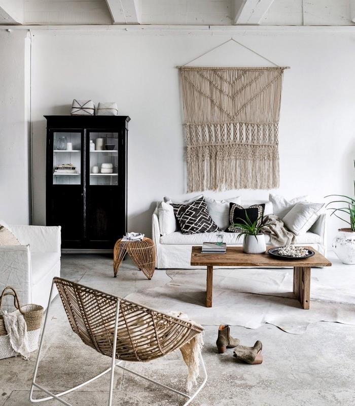 أريكة بيضاء ، لوحة جدارية مكرامية ، خزانة سوداء ، طاولة خشبية ، أرضية أسمنتية ، كرسي بذراعين خشبي