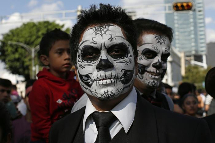 účastníci mexického karnevalu mŕtvych, hlava lebky nakreslená na mužskej tvári, čierna kravata