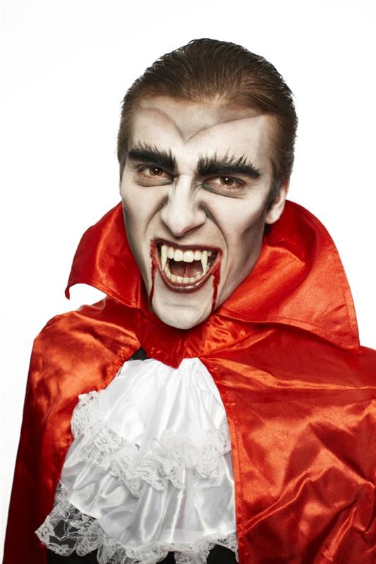 vampyr med falska vampyrtänder och orange cape, blodiga läppar med falskt blod