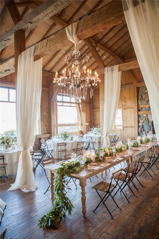 zorganizujte svadbu v starých stodolách s odhalenými trámami, lustrom, priehľadnými bielymi závesmi, drevenými a kovovými stoličkami, ozdobným lístkom a ozdobou držiaka na sviečku