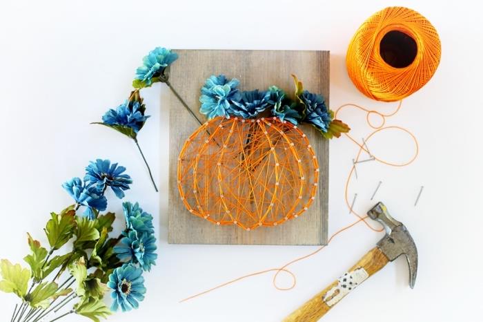 DIY Halloween nápad s krásne ozdobenou drevenou doskou z oranžového napnutého drôtu a modrých umelých kvetov v tvare tekvice