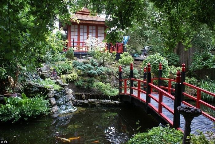 منزل ياباني ، ونباتات منحدرة ، وجسر صغير باللونين الأحمر والأسود ، وبركة كارب كوي صغيرة ، وأشجار وشجيرات