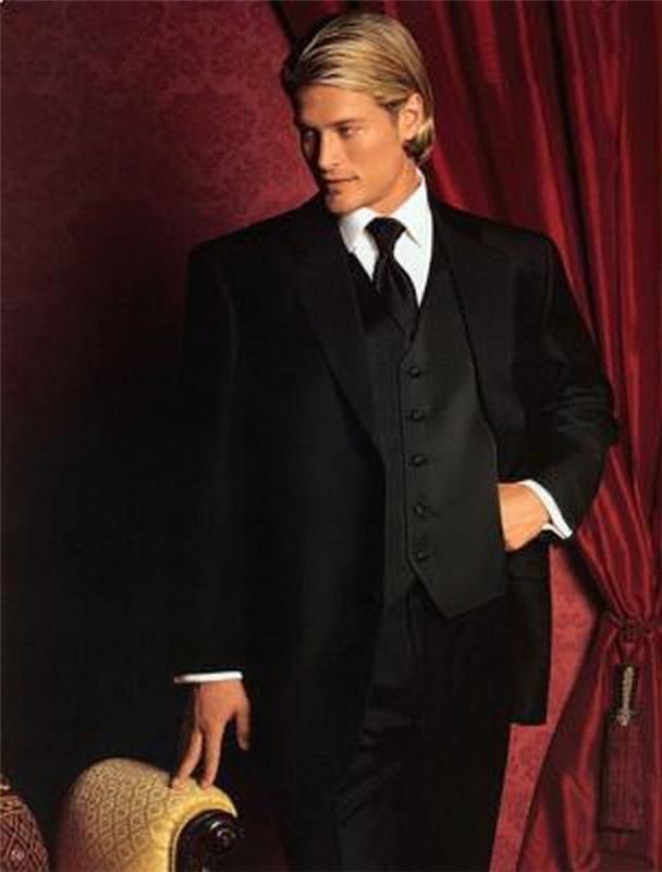 blonďavý muž s vlasmi zastrčenými za ušami, oblečený v čiernom obleku s vestou a kravatou