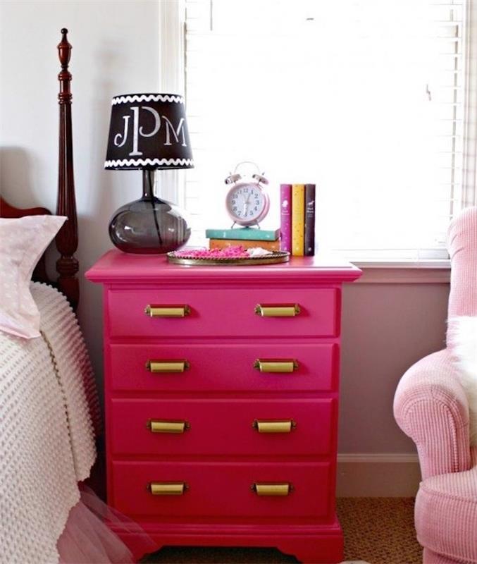 ukážka nábytku premaľovaného na ružovú so zlatými úchytkami na skrini, honosný nočný stolík, knihy, budík, čierna nočná lampa, ružová a biela posteľná bielizeň