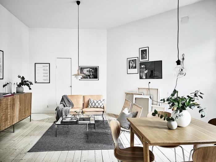 Škandinávsky nábytok v obývačke, sedačka s koženými sedačkami, čiernobiely koberec, drevený stôl a stoličky v jedálni, svetlo sivé parkety, grafická dekorácia na stenu