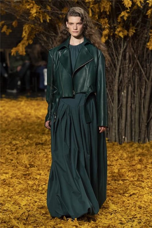 عارضة أزياء تسير على سجادة من أوراق الخريف ، مرتدية فستانًا أخضر داكنًا ، اتجاهات الموضة الخريفية ، سترة جلدية خضراء داكنة