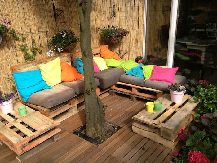 drevená terasa s drevenou pohovkou z palety so sivými podsedákmi a farebnými ozdobnými vankúšmi, malými servisnými stolíkmi v paletách, výhľadom na bambusový vánok