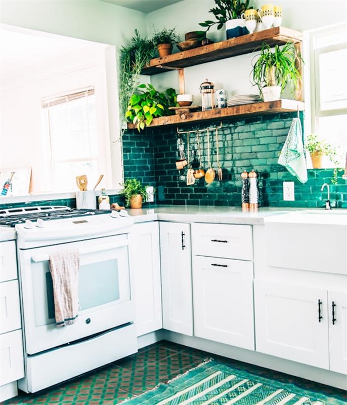 مطبخ أبيض وأخضر بحجم L ، مع خزانة قاعدة بيضاء ، وخزانة من البلاط الأخضر ، وأرفف خشبية ريفية ، وسجاد أخضر وأبيض ، ونباتات خضراء