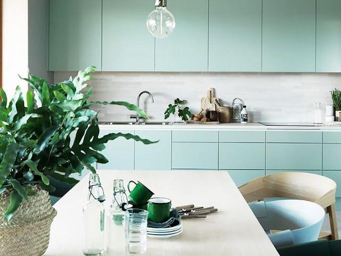 Celadon modrý nápad na fasádu kuchyne, sivý splashback, mramorová pracovná doska, sivobiely stôl, béžové, modré a zelené stoličky, zelené listy rastlín v koši