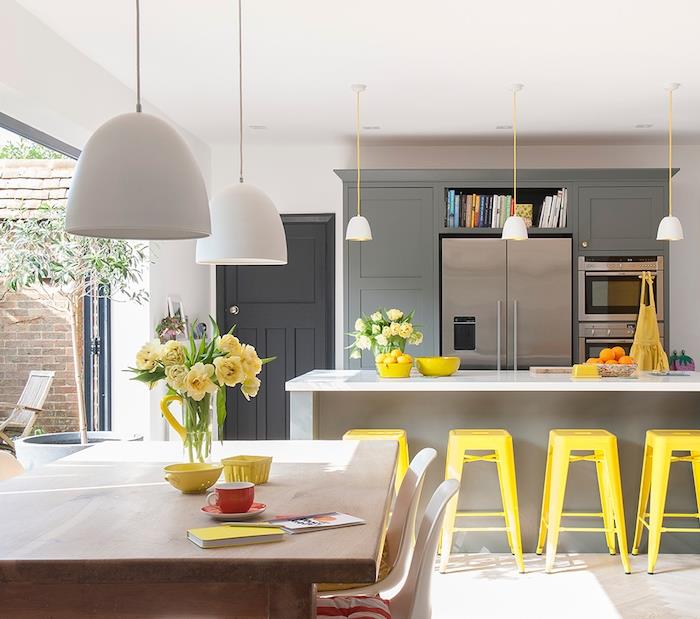 malá otvorená kuchyňa v sivej farbe so sivým barom a žltými metalickými stoličkami sa otvára do jedálne s dreveným stolom a škandinávskymi stoličkami