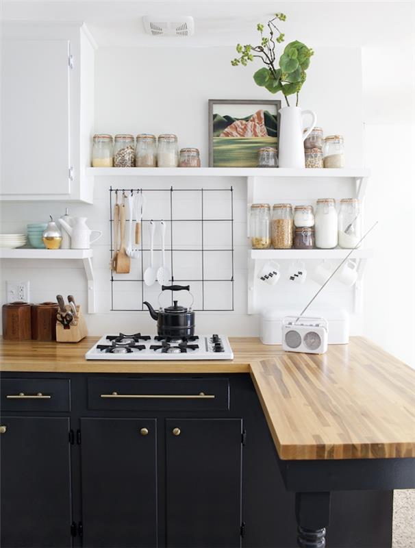 مطبخ تم تجديده بواجهة مطلية باللون الأسود مع مقابض ومقابض ذهبية ، سطح عمل خشبي ، جدار مطبخ أبيض وخزانة ، رف لتخزين برطمانات المكونات