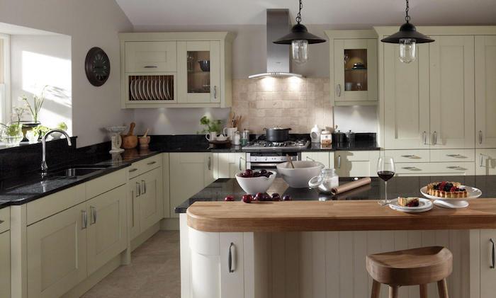 ديكور ريفي بواجهة مطبخ بيضاء اللون وجزيرة خشبية مركزية مع سطح عمل من الجرانيت وأضواء معلقة صناعية
