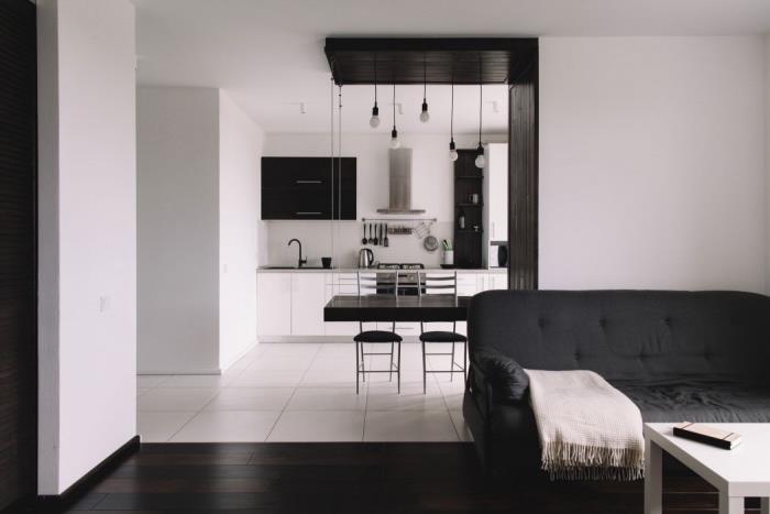 halvöppen köksmodell i svart och vitt, dammsugare i rostfritt stål, svart bord och stolar, vita plattor, mörkt brunt parkett vardagsrum, svart soffa, vitt soffbord