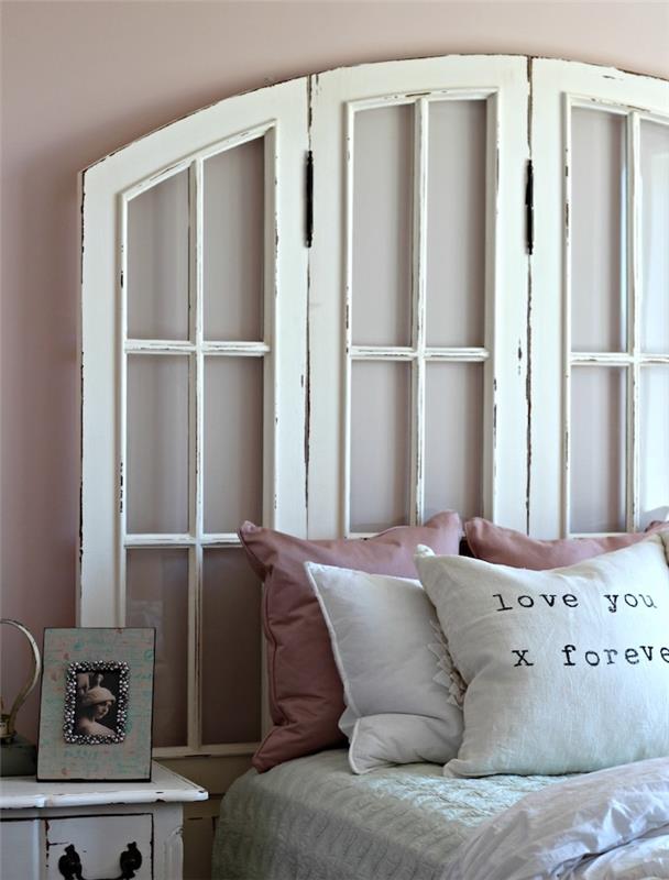vita återvunna vita fönsterluckor, vita sängkläder med rosa dekorativa kuddar, vintage nattduksbord