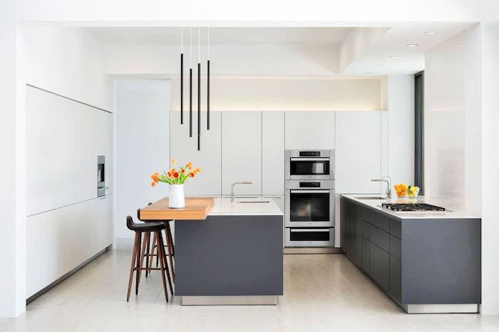 vitt och grått kök med lågt köksskåp och grå centralö och vita bänkskivor, beige klinkergolv, vitt köksskåp, hängande lampor i industriell stil