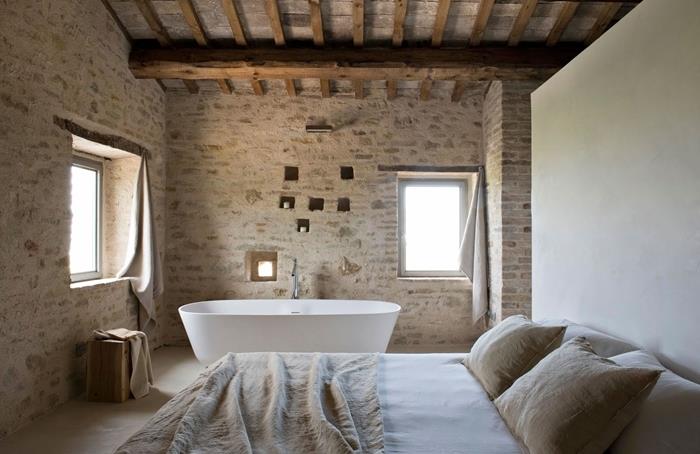 tehlový stenový strop s odhalenými trámami kúpeľňa v spálni voľne stojaca vaňa béžová prikrývka na posteľ