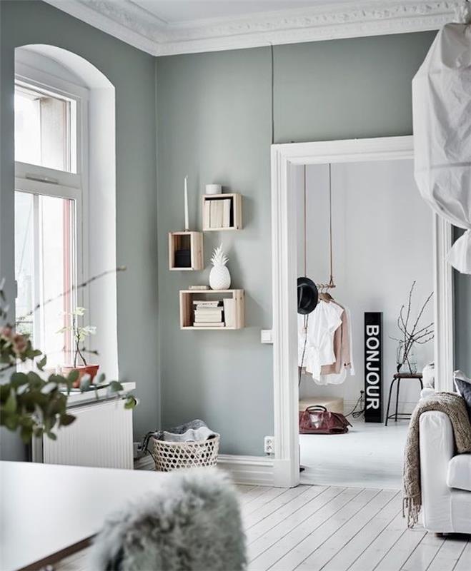 sivozelená stena v škandinávskej obývačke otvorenej do severskej spálne, vybielená parketová podlaha a biela sedačka, drevené police na prepravky, otvorená šatňa