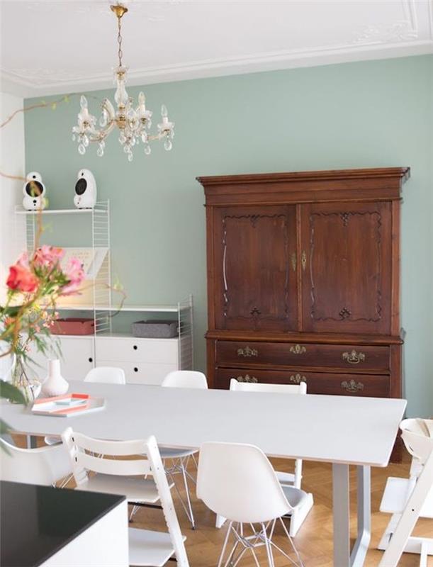 výzdoba jedálne so svetlými seladonovými zelenými stenami, jedálenský stôl a stoličky v škandinávskom štýle, vintage drevená skrinka, elegantný luster