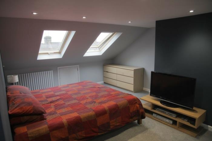 grå väggfärg, röda och bruna sängkläder, tv -skåp, trä byrå, kolgrå accentvägg, beige matta, vindmöbler