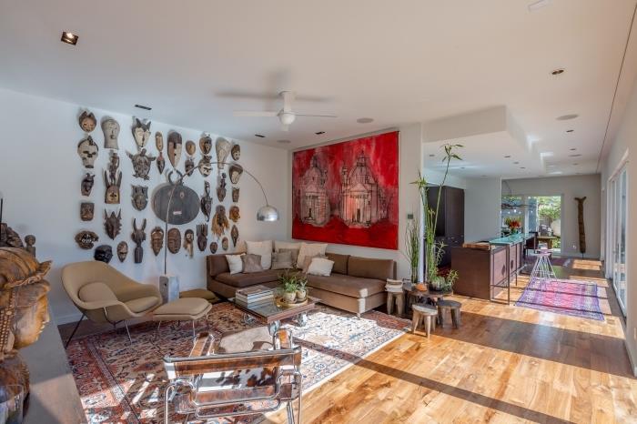 Interiér v africkom štýle v otvorenej obývačke s bielymi stenami s drevenou podlahou a stenou z afrických masiek