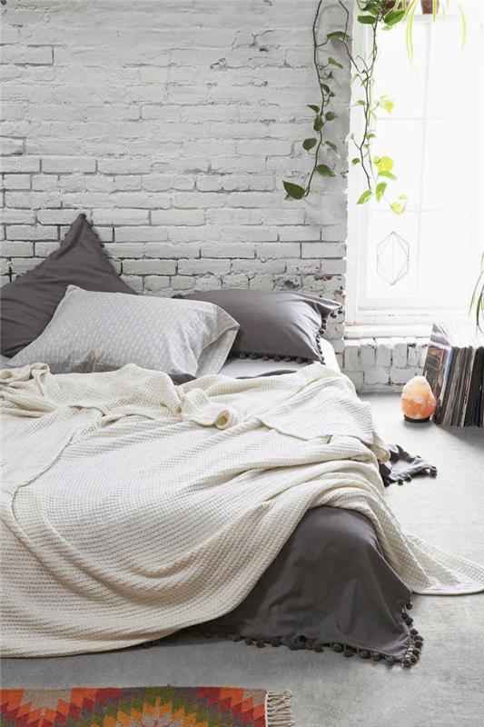 Skandinavisk sovrumslayout, vit tegelvägg, saltljusstake, hängande blomkruka, grå och vit säng