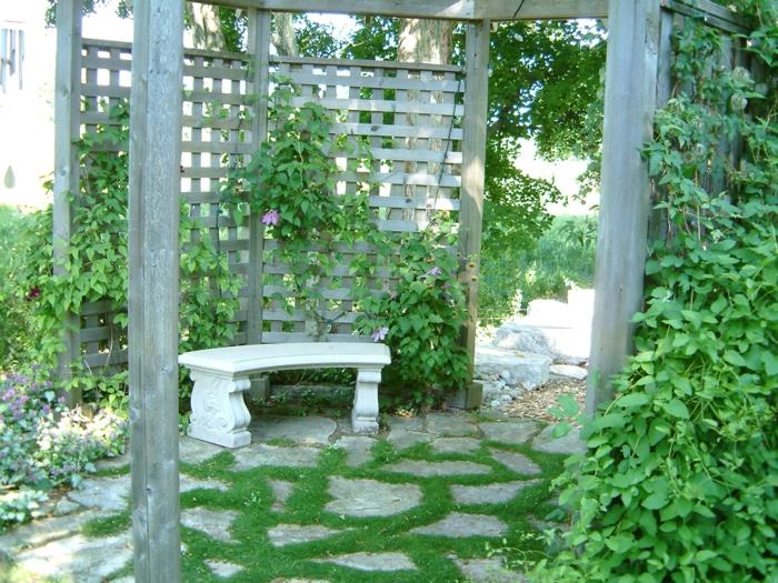 vertikálna záhrada na sivastej drevenej stene, záhradná pavilónová pergola, zem pokrytá veľkými sivými kamienkami obklopená zelenou trávou, vonkajšia zelená stena, zelená stena