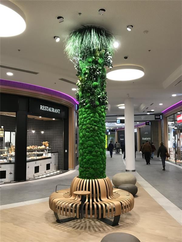 veľké nákupné centrum, dekoratívny stĺp obalený zeleným machom a osvetlený šiestimi bodovými svetlami usporiadanými v kruhu okolo stĺpika, vertikálne pestovanie, zelená stena