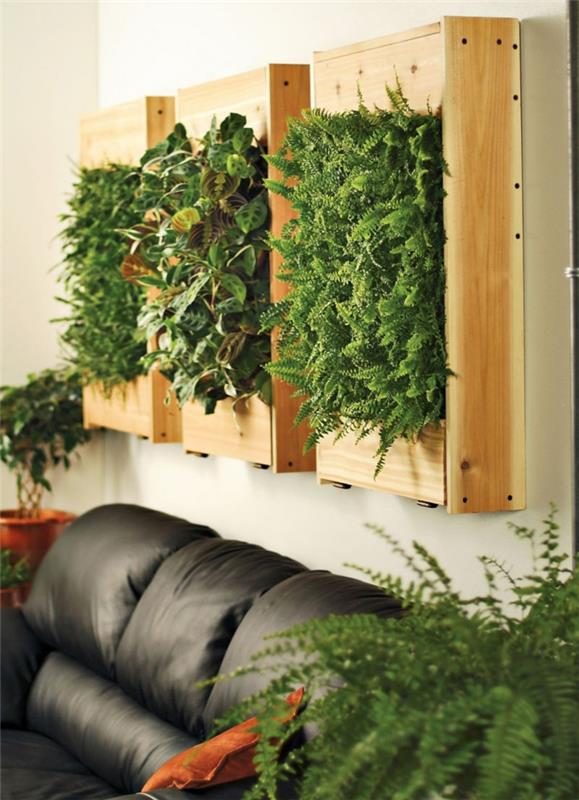 tri panely so svetlými drevenými rámami, paletová zelená stena, mach a nízke zelené rastliny, vnútorná zelená stena, obývačka s čiernou pohovkou z umelej kože