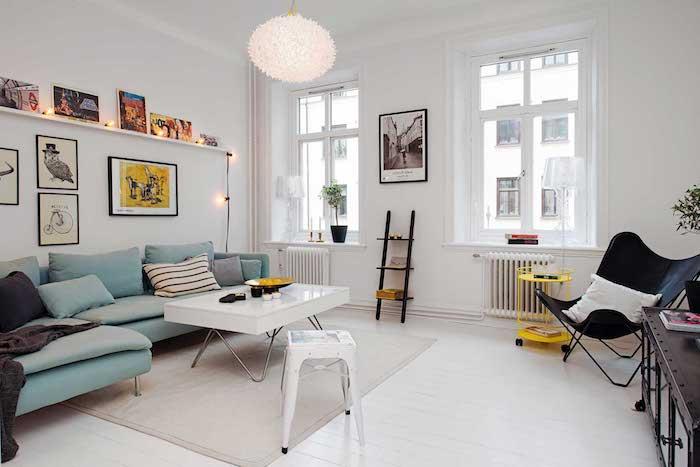 blå hörnsoffa och vitt fällbord bredvid, vita väggar och designerhängande lampa, ekovägg av ramar och ljus krans för skandinavisk kokongdeko