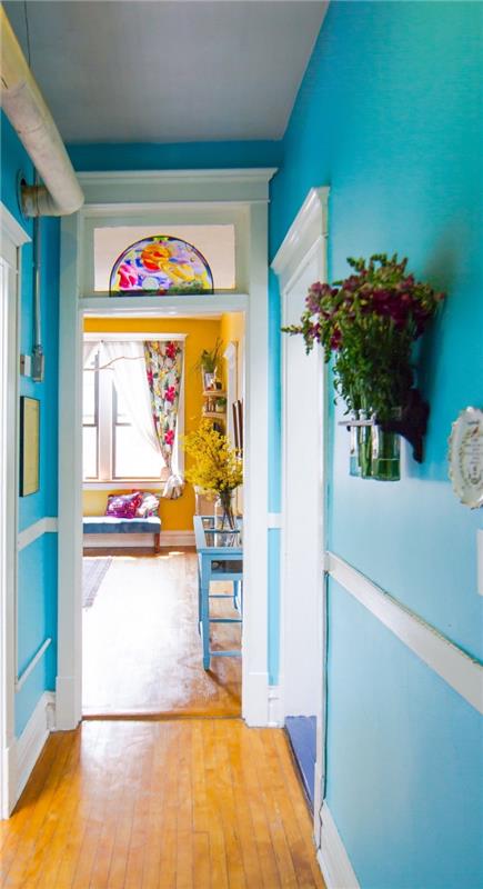 dekorativ smal korridor med väggar målade i ljus turkosblått, med utsikt över ett currygult vardagsrum