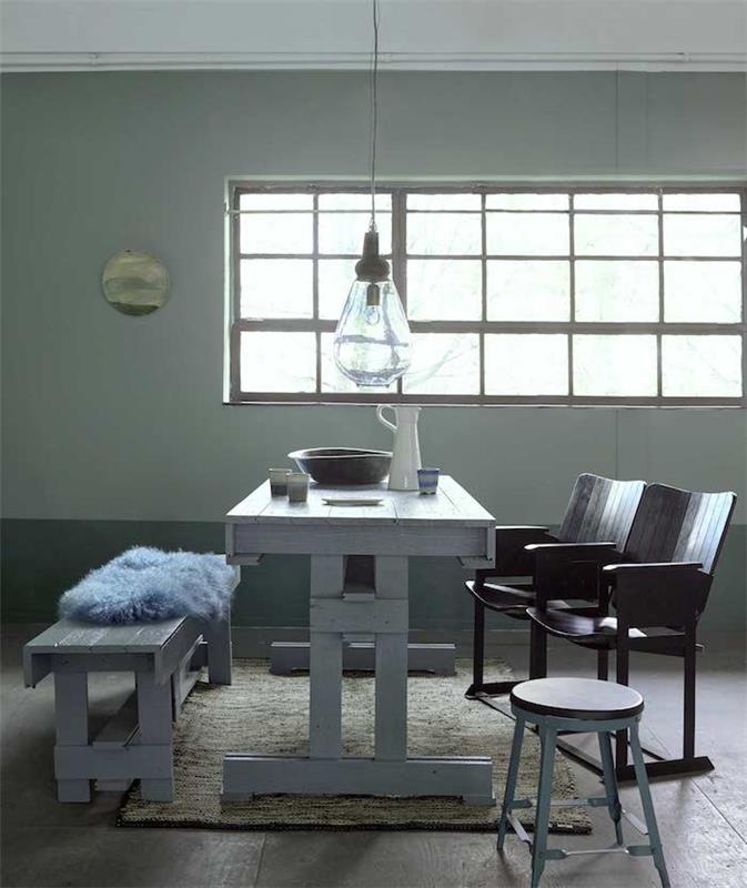 stena zelenej farby, biely stôl a lavica, čierne stoličky zostavené ako lavička, opotrebovaná drevená podlaha, originálne závesné svetlo