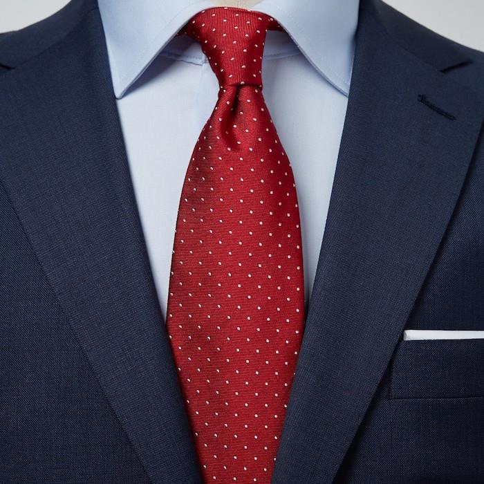 foto av klassisk röd vinröd slips med vita prickar i vindknut på ljusblå skjorta och marin kostym