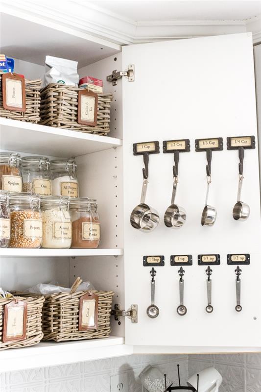 háčiky s malými štítkami na dverách skrine na zavesenie odmerných lyžíc, riešenie vybavenia kuchynskej skrinky pomocou košov a nádob na potraviny