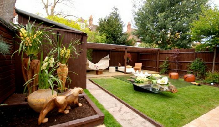 زاوية صغيرة مع العشب الأخضر ، وطاولة قهوة من الزجاج والخشب الطافي ، والمناظر الطبيعية للشرفة ، وفكرة تزيين حديقة الشرفة
