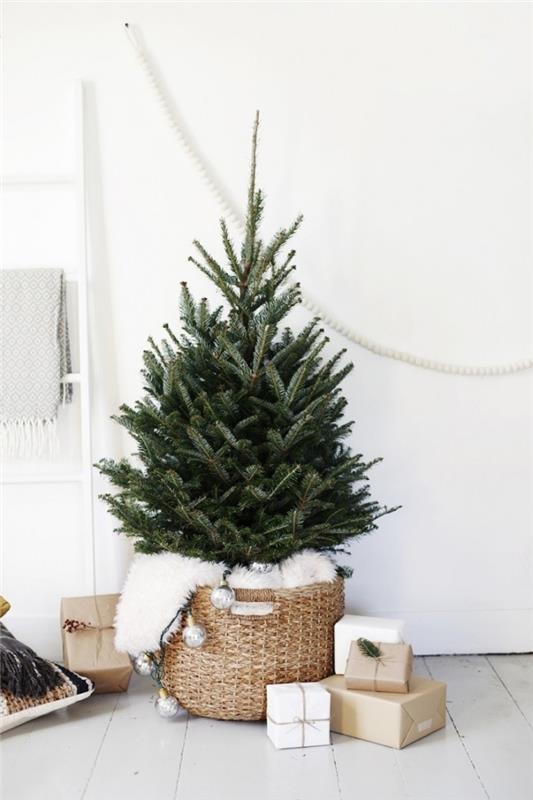minimalistisk julgransdekoration i ett vitt vardagsrum med vit träparkett, julgran i en vävd korg med fluffig pläd